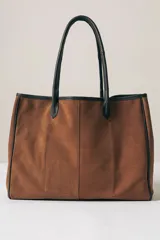 Bolso tipo tote de gamuza color marrón con detalles de bordes y asas en cuero negro.