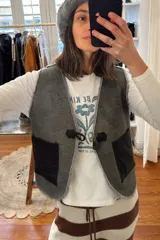 Chaleco reversible confeccionado en cuero genuino. Presenta un lado de piel de oveja gris con bolsillos de cuero negro y un lado de cuero liso gris. Diseño sin mangas con cierre frontal.