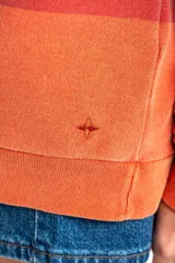 Sweater tipo polo de algodón peinado con diseño de rayas horizontales en tonos rojizos y terracota, cuello camisero y mangas largas con puños.