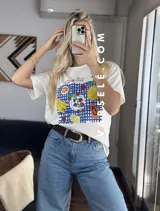 Remera blanca de cuello redondo y manga corta con estampado de frutas sobre un mantel a cuadros azules.