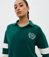 Saco deportivo de modal color verde, con cuello polo, escote en V y mangas largas con franjas blancas horizontales. Presenta un bordado circular en el pecho con la inscripción '94'.