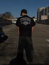 Remera negra de manga corta y corte oversize, con estampa gráfica en blanco en el frente y en la espalda con diseño de tipografía y escudo heráldico.