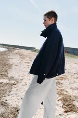 Chaqueta bomber de corte holgado confeccionada en tejido con lana, color azul marino. Presenta cuello subido, cierre frontal con cremallera metálica, bolsillos delanteros y detalle de trabillas con botones metálicos en el ruedo.