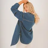 Camisa de jean celeste con botones blancos, corte holgado, mangas largas y bolsillos frontales.