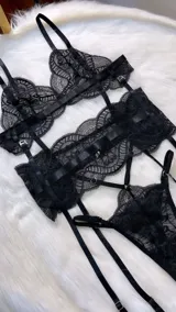 Conjunto de lencería de cuatro piezas en encaje negro. Incluye bralette con breteles regulables, tanga con tiras dobles ajustables en la cintura, portaligas con enganches desmontables y ligas para las piernas.
