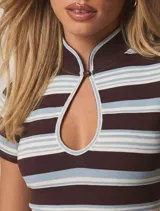 Top de mangas cortas con diseño de rayas horizontales en tonos marrón, blanco y celeste. Presenta un cuello alto con cierre de botón y una abertura frontal tipo cut-out en el pecho.