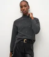 Suéter de punto color negro con cuello medio estructurado y mangas largas. Presenta un patrón geométrico sutil y aplicación de beads distribuidos por toda la parte frontal.