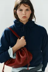 Mini bolso de hombro en color bordó con textura efecto reptil, diseño fruncido con cordones ajustables en los laterales y una sola asa superior.