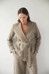 Chaqueta corta color beige, entallada, con escote en V, manga larga y bolsillos escondidos. Cierre frontal con lazo fijo. Confeccionada en lana fina sin teñir. Diseño exclusivo de Don Baez.