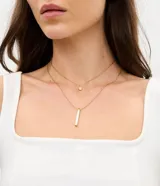 Collar doble en capas de acero inoxidable dorado, compuesto por una cadena corta con dije redondo pequeño y una cadena larga con dije rectangular alargado con incrustación de nácar.