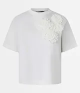 Remera blanca de algodón con cuello redondo y corte boxy, con apliques de flores de tejido en relieve en la zona del pecho.
