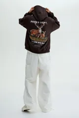 Canguro de mezcla de algodón color marrón oscuro, con capucha cruzada, bolsillo canguro frontal y puños y bajo acanalados. Presenta un estampado pequeño en el pecho con texto y símbolos.