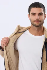 Campera de corderito color beige con interior de polar, cierre frontal completo y bolsillo vertical en el pecho con borde en contraste azul marino.