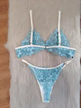 Conjunto de lencería compuesto por un corpiño triangular y una bombacha, confeccionados en encaje floral color aguamarina con detalles de ribetes en color champagne. El corpiño cuenta con breteles regulables y la bombacha presenta laterales ajustables.