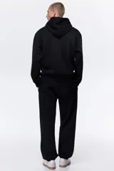 Pantalón deportivo negro de felpa con interior cepillado suave. Modelo de corte relajado con elástico revestido y cordón ajustable en la cintura, bolsillos laterales y puños acanalados.