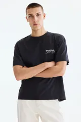 Remera negra de algodón con cuello redondo acanalado y mangas cortas de hombros caídos. Presenta un pequeño estampado tipográfico en el pecho con las palabras "No Defeat Just Glory".