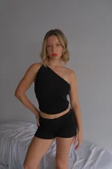 Top negro de manga única (one-shoulder) con efecto drapeado en el torso, confeccionado en tela de licra/lúrex.