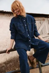Sobrecamisa de jean color azul oscuro, con corte oversize, cuello clásico, cierre frontal con botones metálicos y dos bolsillos frontales tipo parche.