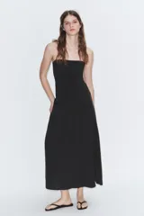 Vestido largo de color negro con cuello halter y escote recto. Presenta un diseño fluido con cierre de cremallera oculta en la espalda y lazada ajustable en el cuello.