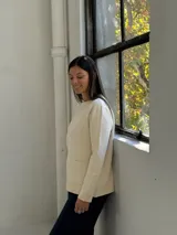 Sweater de punto color beige, con cuello redondo, manga larga y dos bolsillos frontales tipo parche.