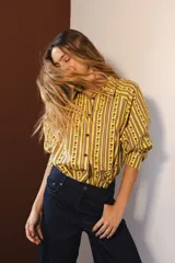 Camisa de manga larga con cuello clásico y cierre frontal de botones. Presenta un diseño de rayas verticales verdes y blancas con un estampado lineal de pequeñas flores rojas.
