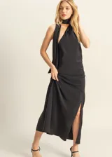 Vestido largo de satén negro con cuello halter, espalda descubierta con detalle de lazo y tajo lateral en la falda.