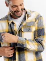 Sobrecamisa de franela con diseño a cuadros en tonos amarillo, gris y blanco. Presenta cuello clásico, cierre frontal con botones, mangas largas con puños abotonados y un bolsillo frontal con solapa.