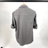 Camisa gris de manga larga con puños enrollados, cuello clásico y cierre con botones.