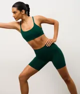 Bermuda tipo biker de tiro alto, confeccionada en microfibra técnica color verde oscuro. Presenta un diseño ajustado al cuerpo con bolsillo lateral funcional integrado, ideal para actividades deportivas.