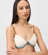 Top de bikini de media copa con aro, confeccionado en microfibra texturizada color blanco con detalles en celeste y tirantes finos marrones. Cuenta con un pequeño aplique metálico decorativo en el centro.
