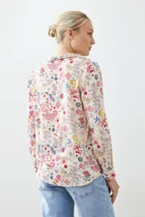 Camisa de manga larga con cuello clásico y estampado floral multicolor sobre fondo blanco.