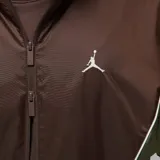 Campera rompevientos Nike Jordan con diseño color block en tonos marrón y verde oliva. Presenta cierre frontal completo, capucha ajustable, bolsillos laterales con cierre y logo Jumpman bordado en el pecho.