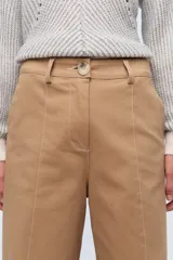 Pantalón de vestir color crema, de corte ancho y tiro alto. Se ajusta a la cintura con cinturón de cuero marrón.