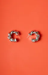 Aro tipo argolla de metal plateado con diseño trenzado.