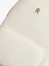 Mochila Tommy Hilfiger de nailon color beige, con diseño curvo, bolsillo frontal con cierre y detalles en cuero sintético marrón en el asa superior. Cuenta con el monograma TH metálico dorado en la parte delantera y correas ajustables.