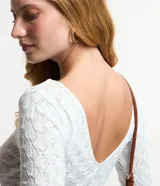 Blusa de manga larga, color blanco, con cuello redondo y textura de punto calado con diseño geométrico.