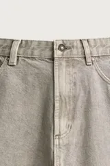 Pantalón barrel fit de mezclilla color verde militar, con efecto lavado, cinco bolsillos, cierre frontal con cremallera y botón, y detalle de pinzas en las rodillas.
