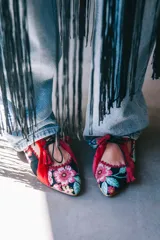 Zapatos tipo blucher de diseño artesanal, confeccionados en algodón con estampado floral multicolor sobre base negra. Presentan detalles en terciopelo color fresa, cierre con cordones rematados en borlas y suela de cuero.
