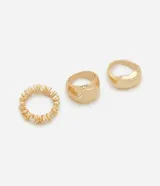 Set de tres anillos de metal dorado con diseños variados: uno con textura radial tipo flor y dos modelos de superficie irregular y robusta.