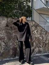 Conjunto de dos piezas negro de tejido acanalado, compuesto por un suéter holgado con cuello polo y mangas largas amplias, y un pantalón largo de corte recto y holgado.