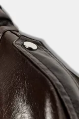 Cazadora de piel 100% de color marrón oscuro, con cuello subido, manga larga con puño elástico y bolsillos frontales con solapa. Presenta cierre frontal con cremallera y botones a presión.