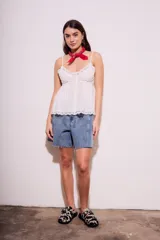 Blusa negra de algodón con tirantes finos, escote en V decorado con encaje y cierre frontal con botones. Presenta un corte holgado con detalles de encaje en el borde inferior.