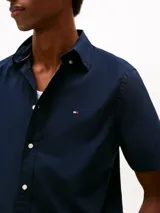 Camisa de manga corta Tommy Hilfiger en color azul marino, confeccionada en tejido popelina con tecnología flex. Presenta cuello clásico, cierre frontal con botones y el logo de la marca bordado en el pecho.