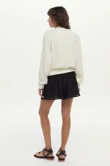 Sweater de tejido de punto color blanco marfil, con calce relajado, mangas largas levemente abullonadas, escote en V con botones y detalles de ribetes en color negro.
