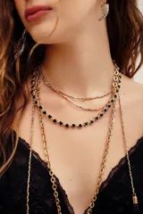 Collar dorado de múltiples tiras, compuesto por una cadena delicada con pequeños abalorios y otra cadena decorada con apliques en forma de corazón con detalles negros.