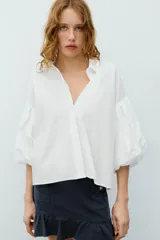 Camisa roja de cuello solapa, con mangas cortas abullonadas tipo globo y cierre frontal con botones ocultos.