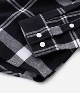 Camisa de franela de manga larga con estampado de cuadros en blanco y negro. Presenta cuello inglés, cierre frontal con botones y bolsillo en el pecho.