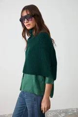Capita de punto acanalado en color verde oscuro, con cuello alto y diseño corto que cubre hombros y pecho.