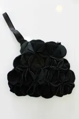 Cartera de mano verde oscuro hecha de círculos de lana merino afieltrada teñida artesanalmente, con asa de cuero marrón.