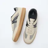 Zapatillas urbanas de malla y ante sintético en tonos beige y negro, con suela de goma marrón y cordones claros.